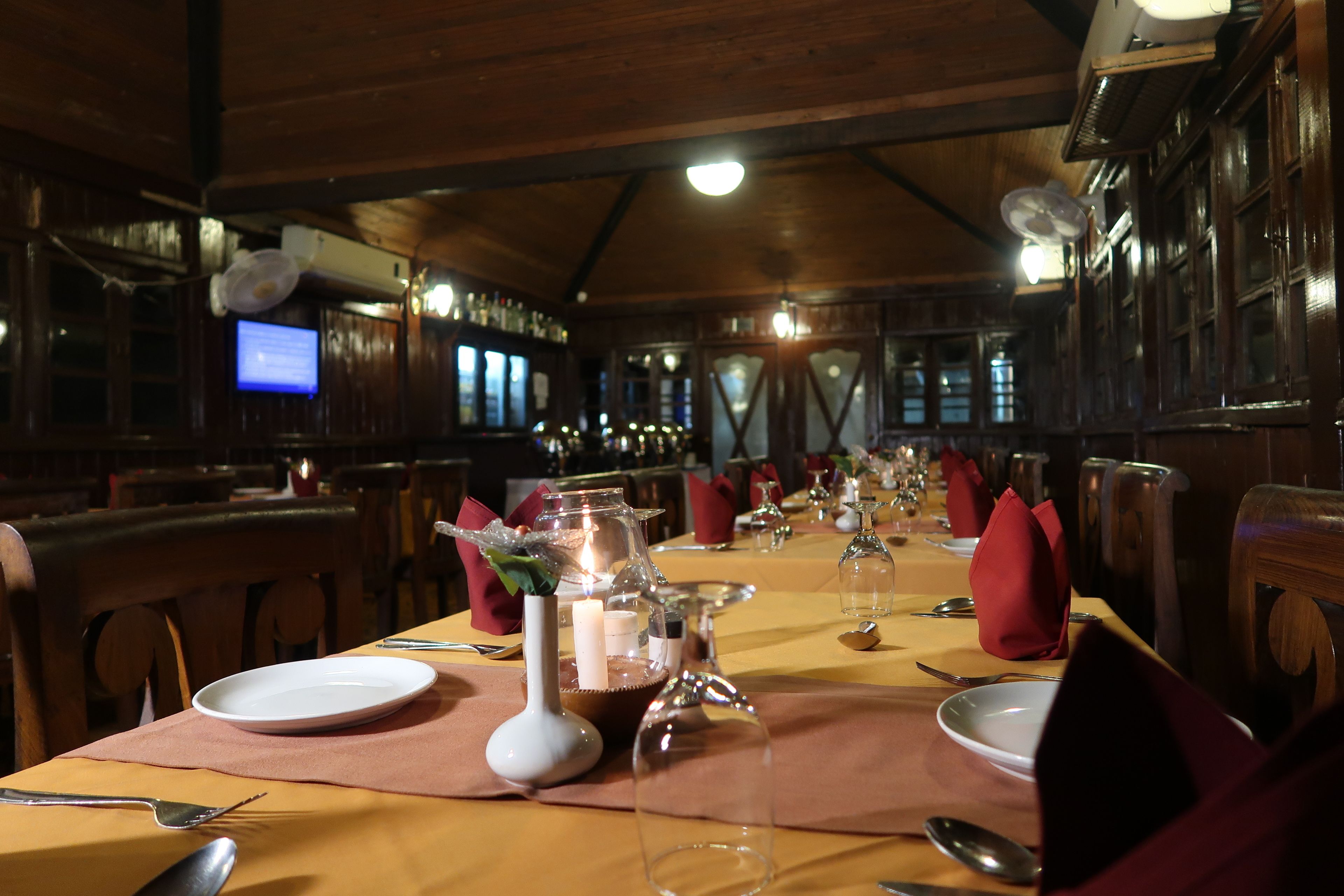 Un restaurante con interiores de madera, mesas dispuestas con platos, cubiertos y servilletas rojas.
