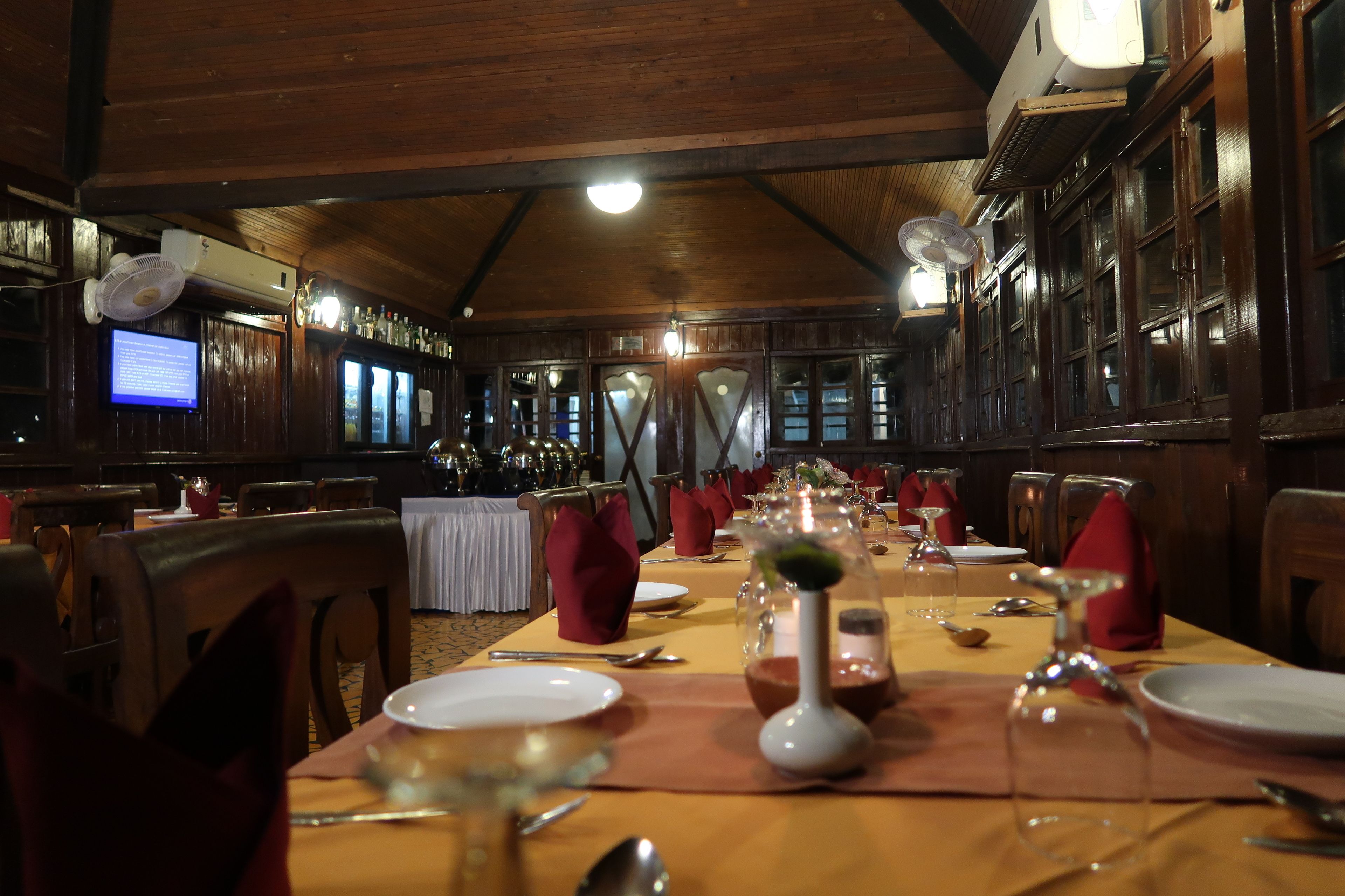 Un restaurante con interiores de madera, mesas dispuestas con servilletas rojas, copas de vino y cubiertos.