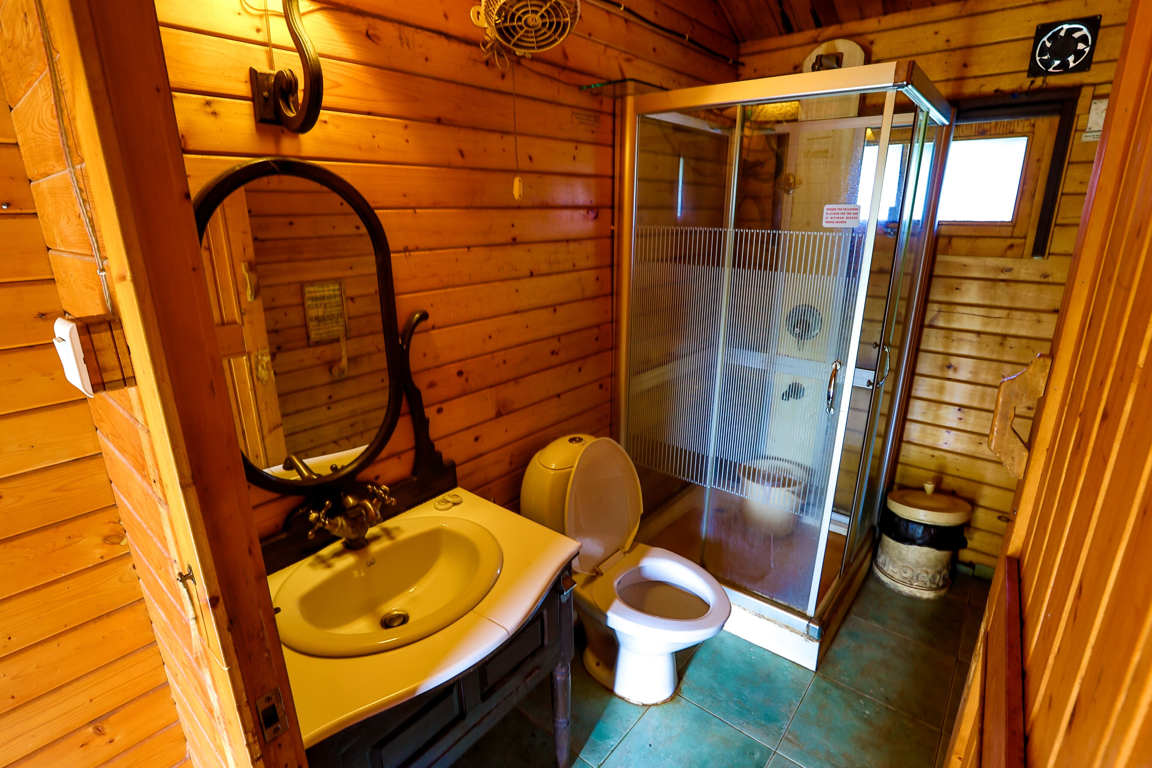 A wooden cabin bathroom with a sink, toilet, and glass-enclosed shower.