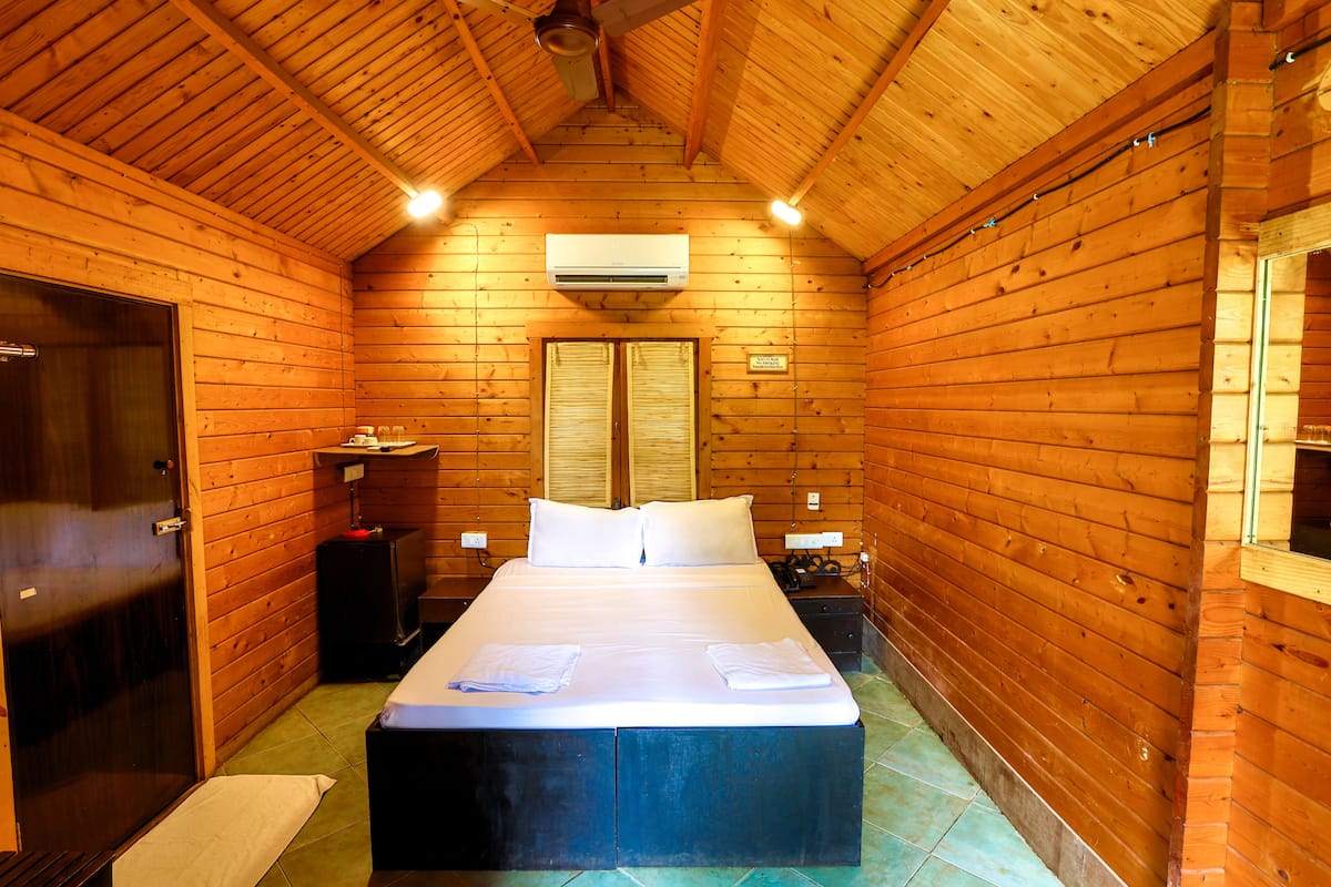 A wooden cabin room with a bed, a desk, and a wardrobe.