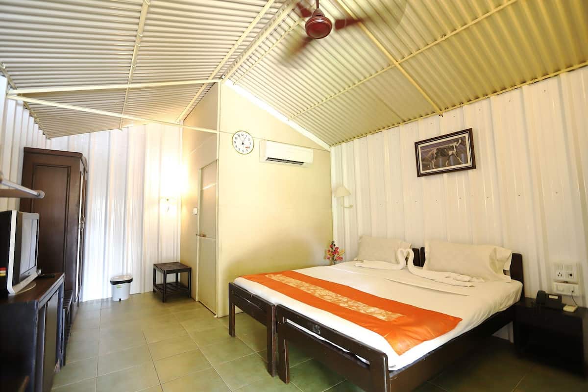 A hotel room with a bed, a television, an air conditioning unit, a clock, and a framed picture on the wall.