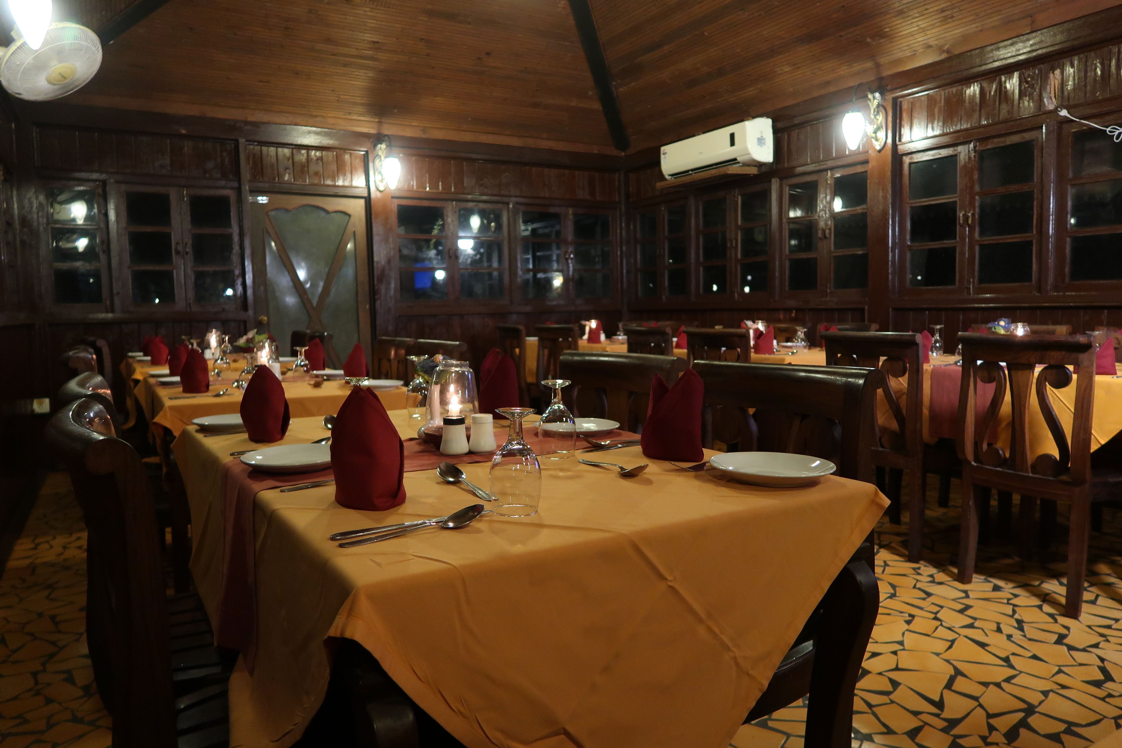 Un restaurante con interior de madera, mesas dispuestas con servilletas rojas y suelo de baldosas.