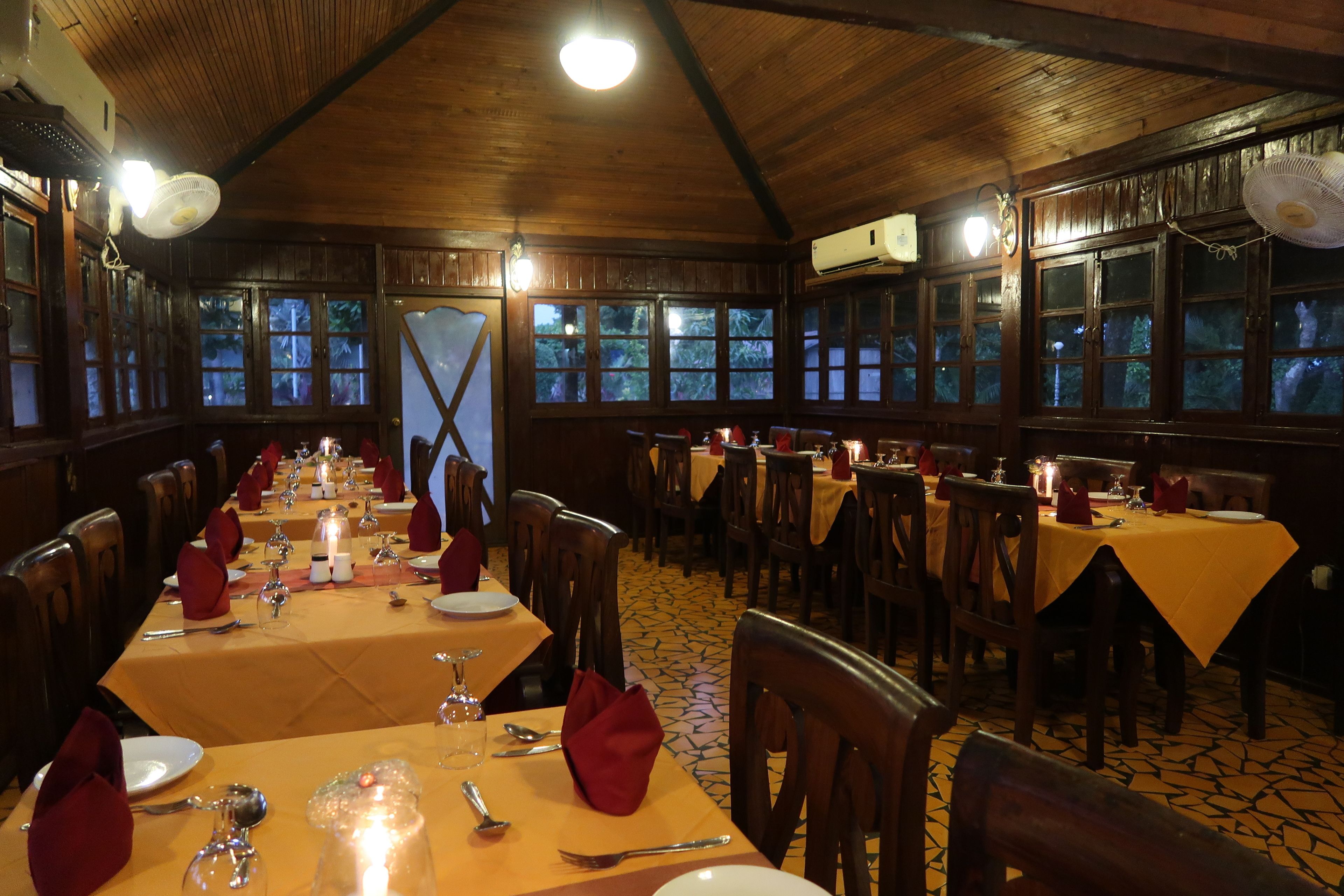 A restaurant with wooden interiors, multiple tables set for dining, and large windows.