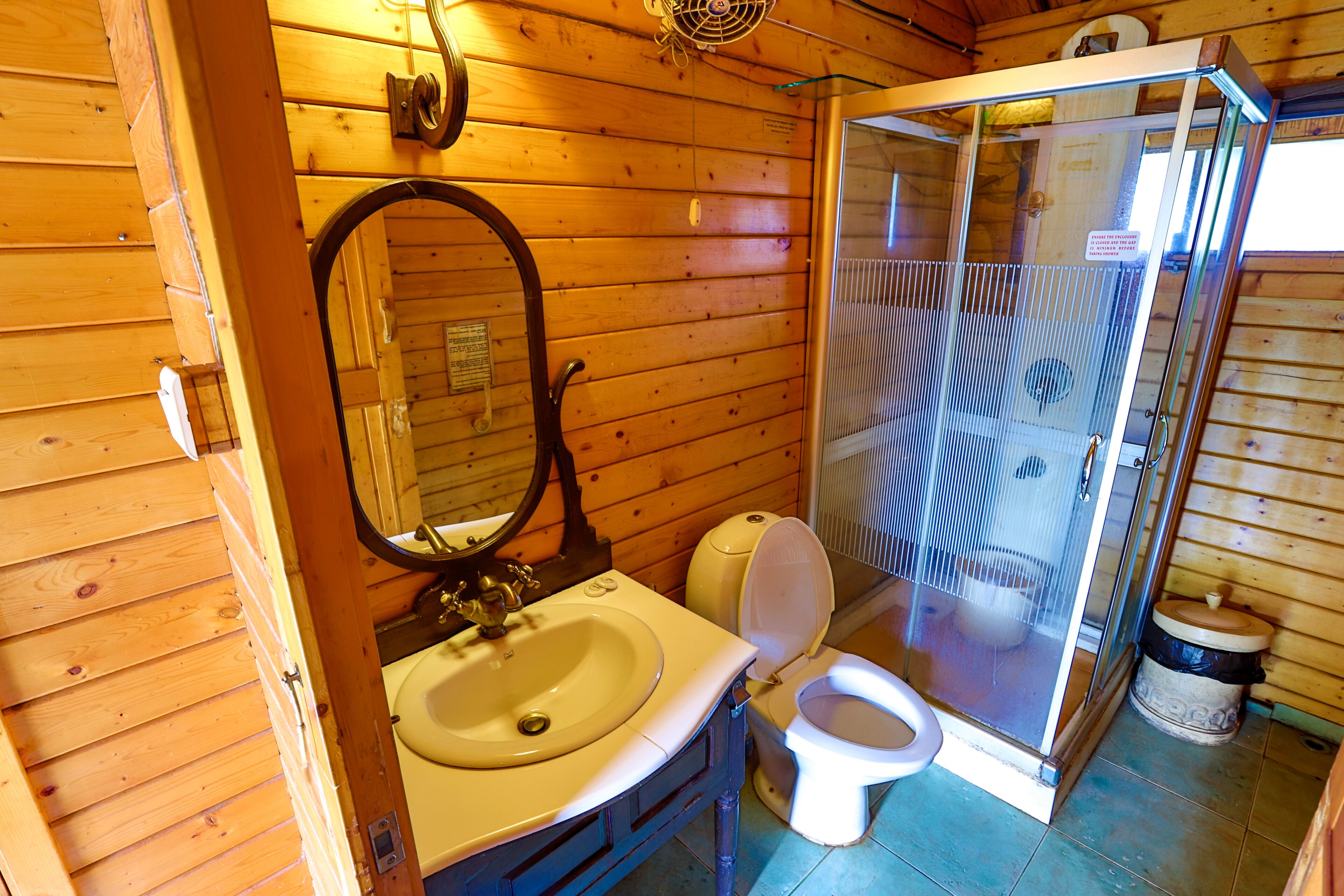 Baño de cabaña de madera con lavamanos, inodoro y ducha con cerramiento de vidrio.