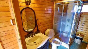Baño de cabaña de madera con lavamanos, inodoro y ducha con cerramiento de vidrio.