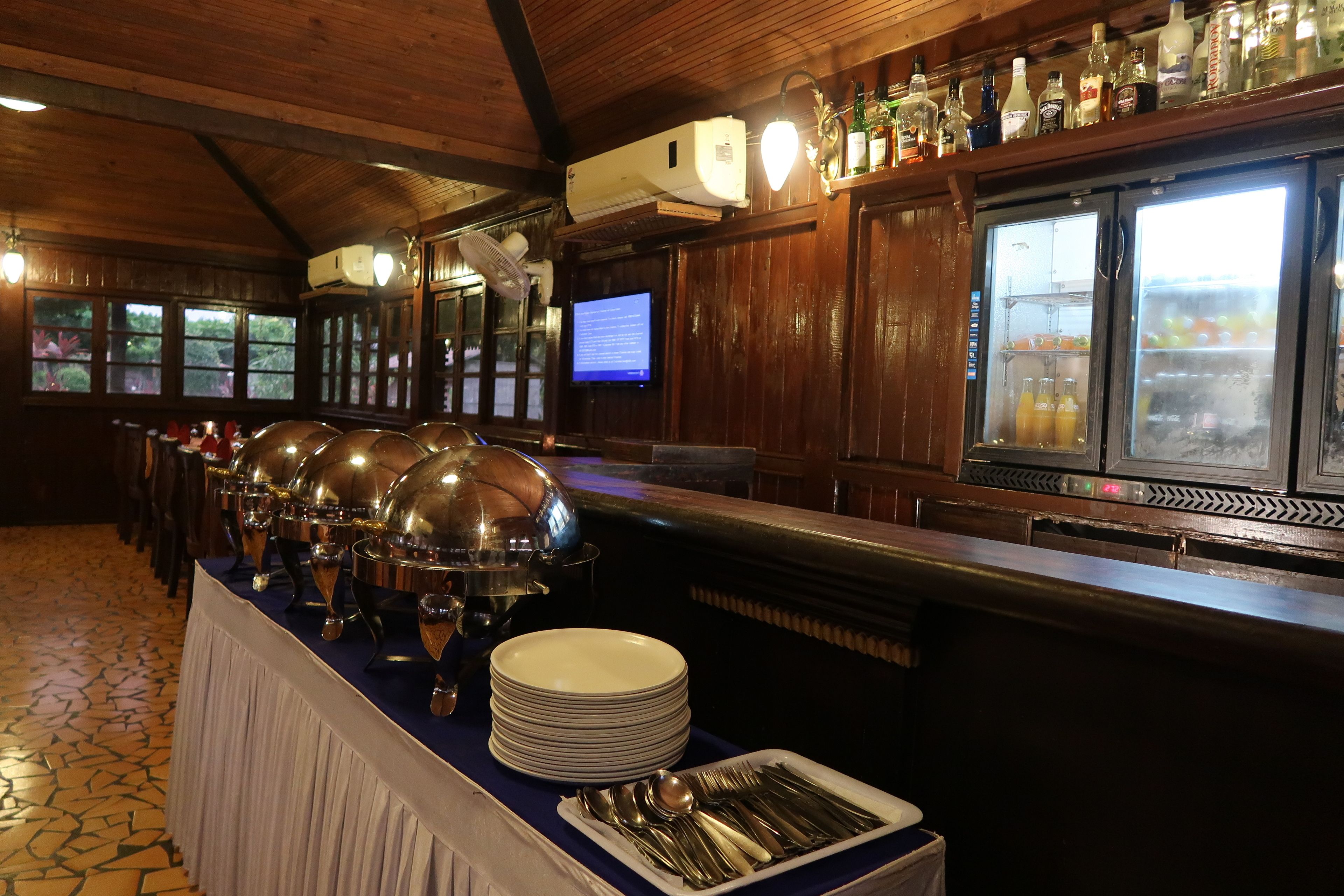 Uma mesa de buffet com pratos tampados, um refrigerador para bebidas e uma tela de televisão.