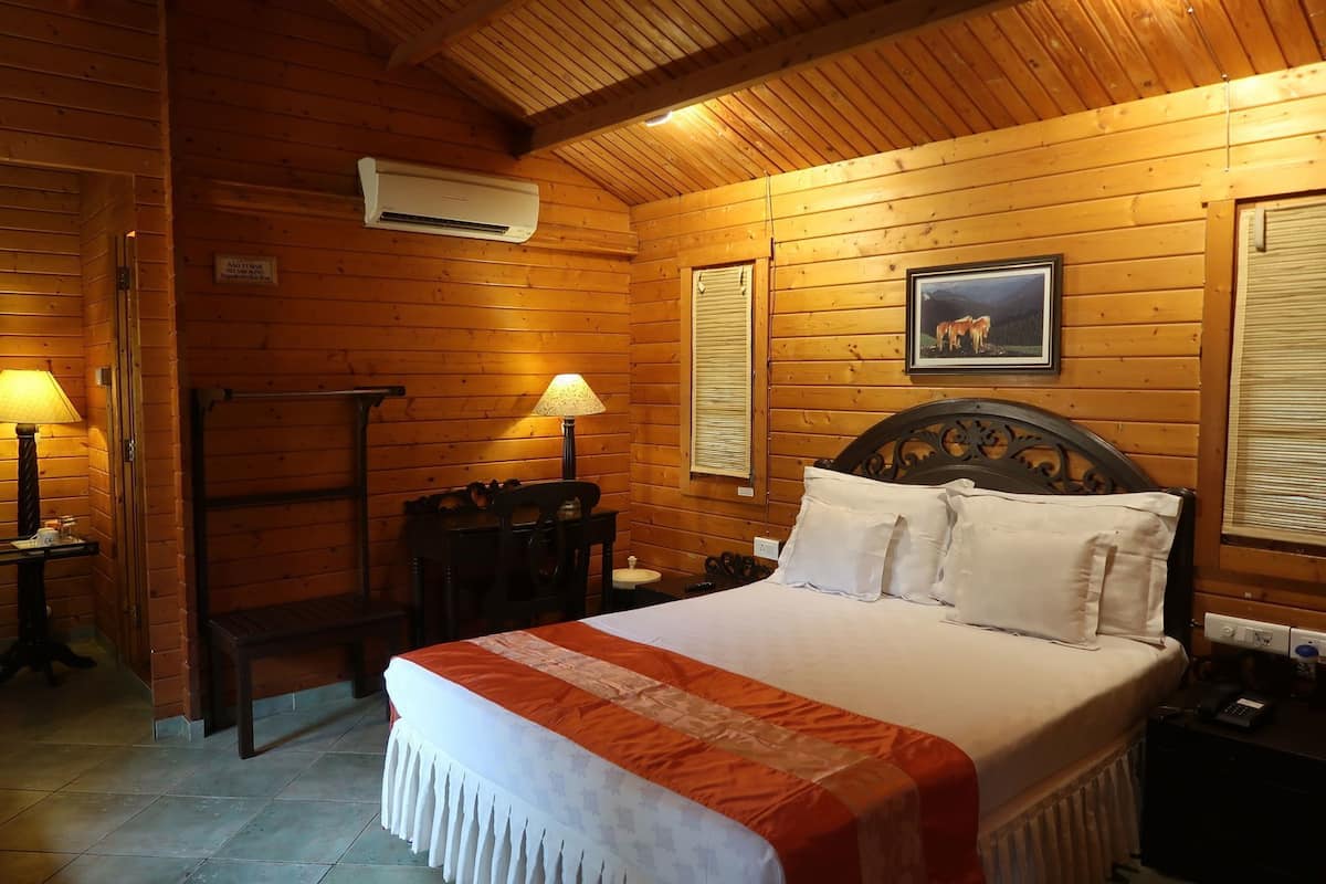 A wooden-paneled room with a bed, two lamps, a picture on the wall, and an air conditioning unit.