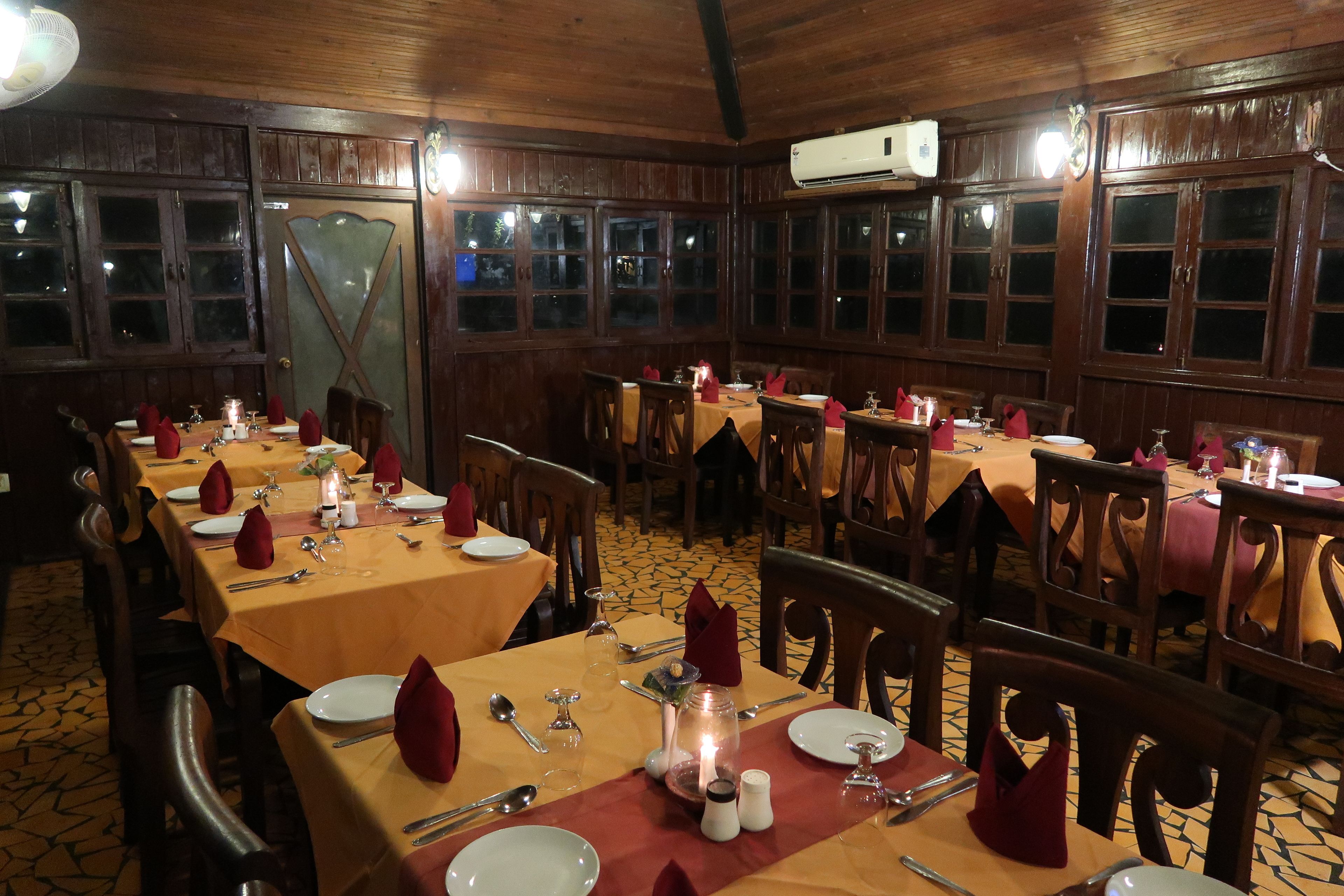 Un restaurante con paneles de madera, varias mesas dispuestas con servilletas rojas, platos y cubiertos.