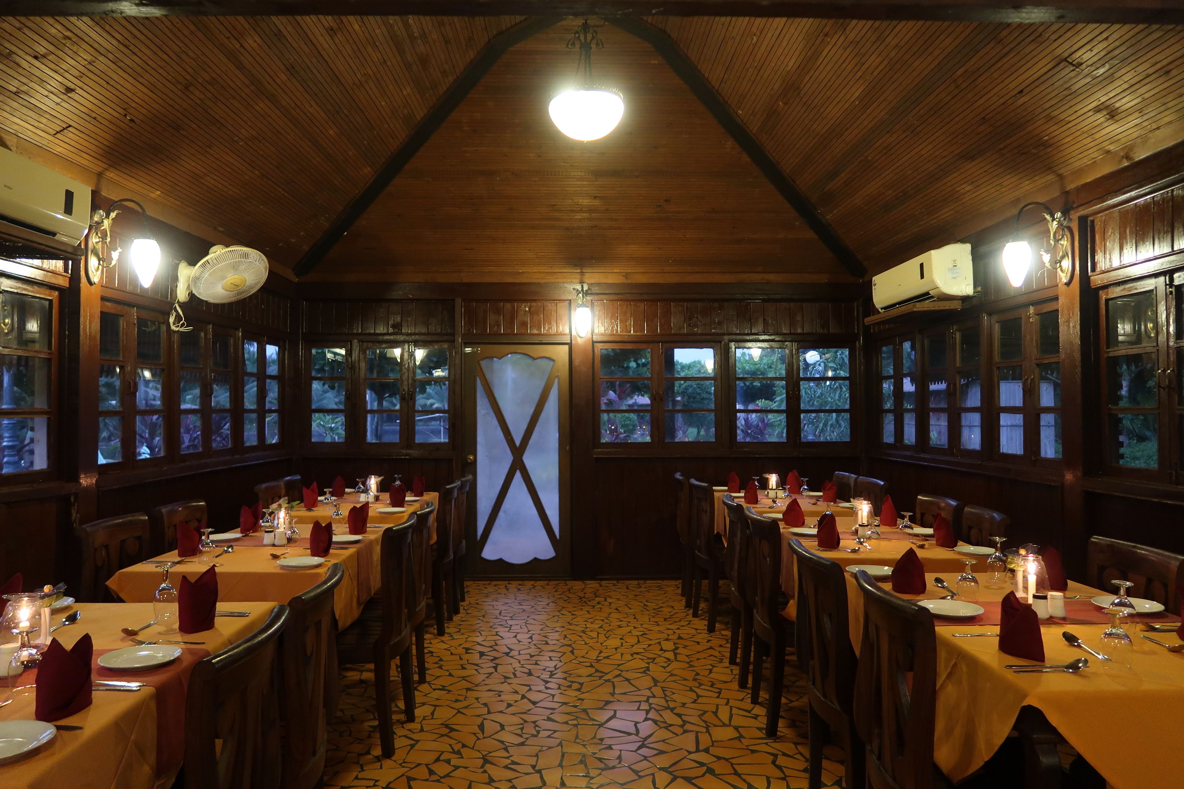 A dining area with wooden tables and chairs, a tiled floor, and a wooden ceiling with a light fixture.