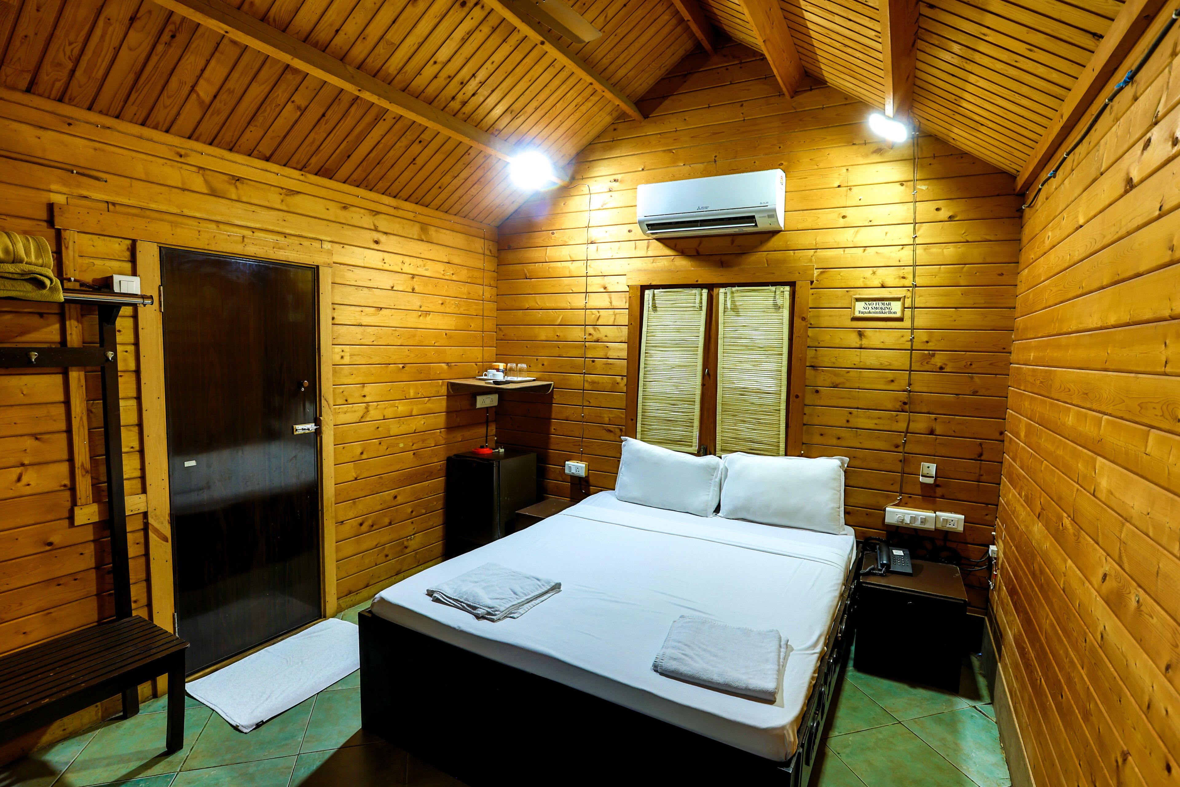 Habitación de cabaña de madera con cama, un banco, una mesita, un televisor y un equipo de aire acondicionado.