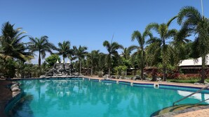 A clear blue pool surrounded by palm trees and a rocky waterfall feature. - Resort Primo Bom Terra Verde (Baga)