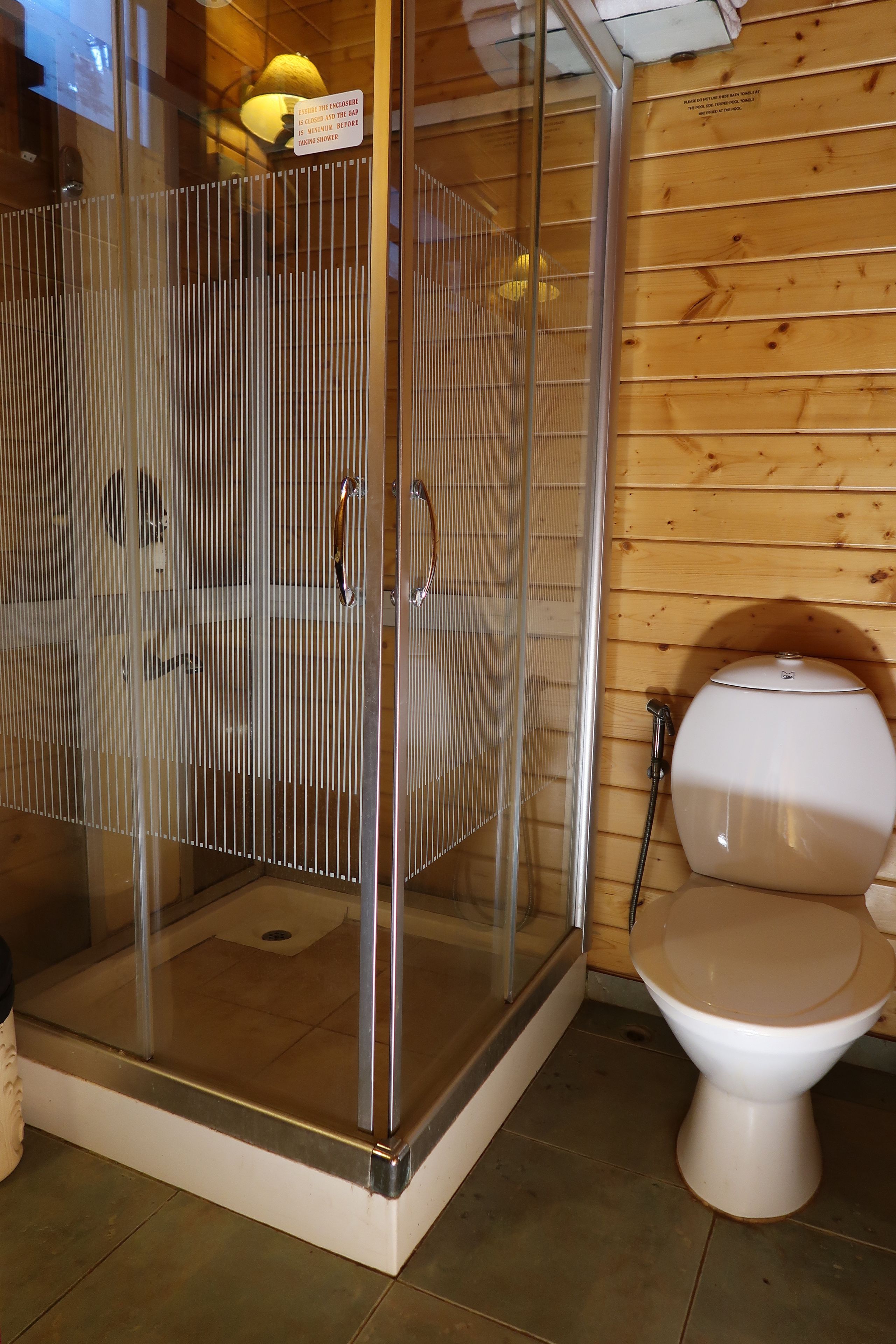 A shower enclosure with a glass door, a toilet, and wooden paneling on the walls.
