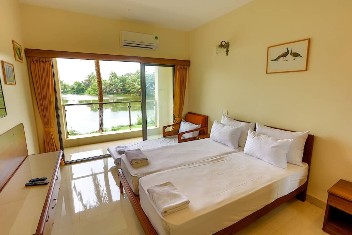 A hotel room with two beds, a desk, a chair, and a large window with a view of a lake.