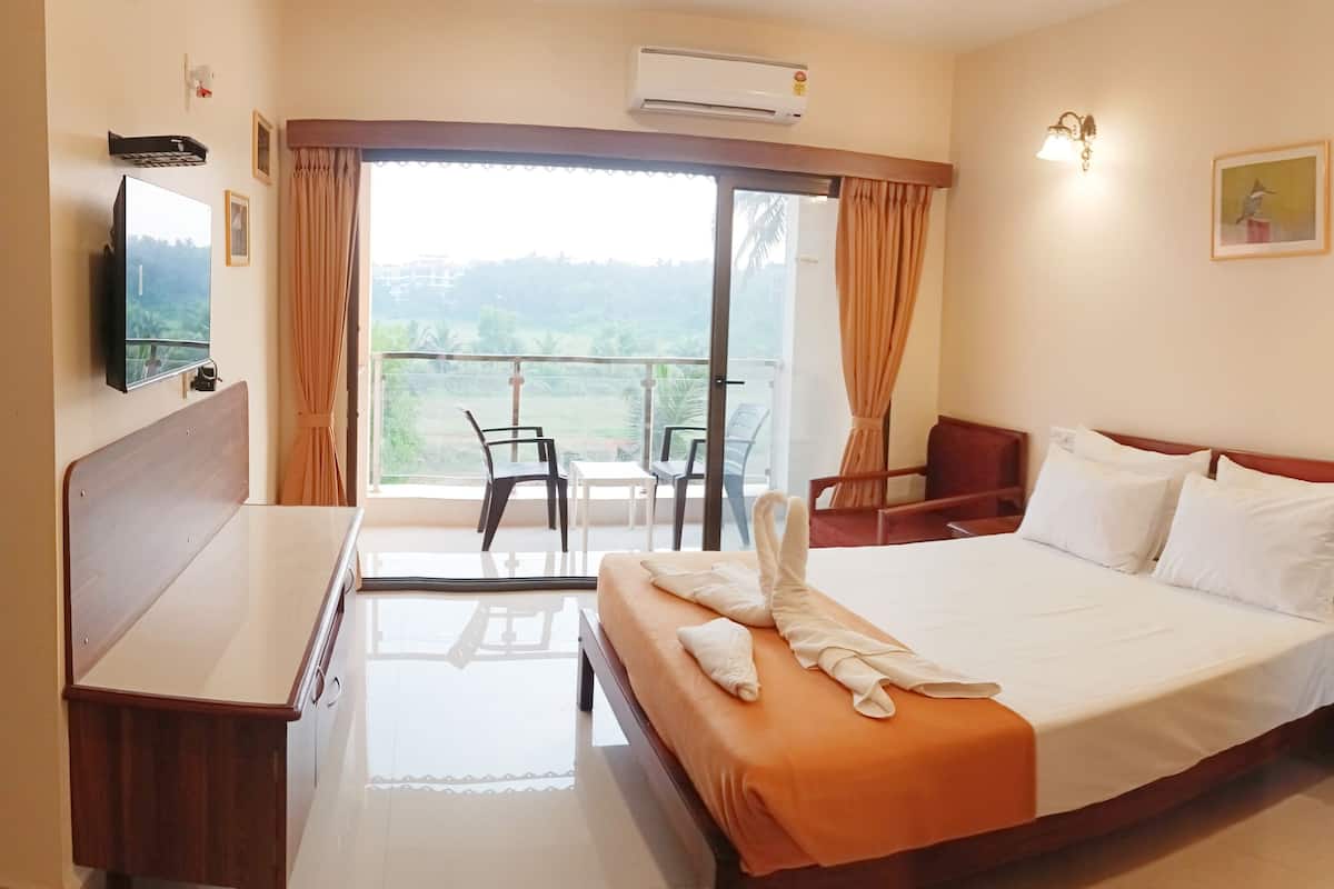 A hotel room with a bed, a desk, a chair, a balcony with a view, and a mounted TV.