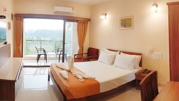 A hotel room with a bed, a desk, a chair, a balcony with a view, and a mounted TV.