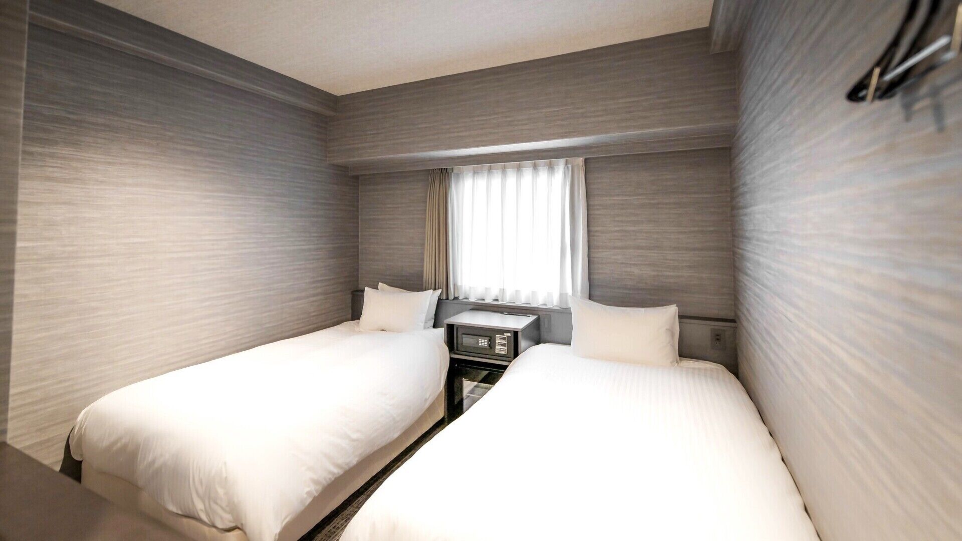 Una habitación de hotel con dos camas, una mesita de noche y una ventana con cortinas.