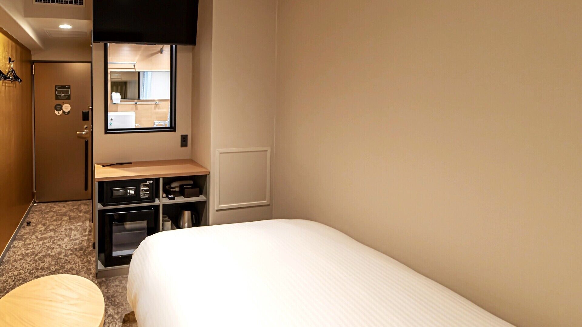 Habitación de hotel con una cama, un escritorio pequeño con una computadora, un espejo y una puerta al baño.