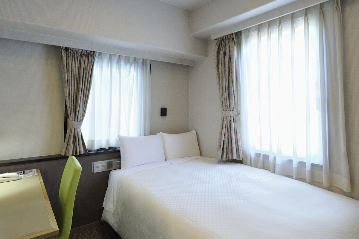 Une chambre d’hôtel avec un lit, un bureau et deux fenêtres équipées de rideaux.