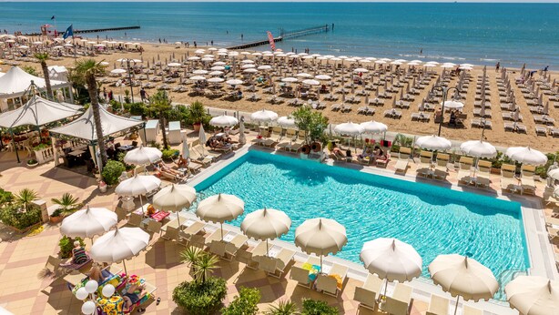 A resort with a large pool surrounded by sun loungers and umbrellas, a beach area with umbrellas and lounge chairs, and a pier extending into the sea. - Luxor e Cairo The Beach Resort (Jesolo)
