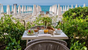 A table set for breakfast with a view of the beach and umbrellas in the background. - Luxor e Cairo The Beach Resort (Jesolo)