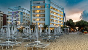 A hotel with multiple floors, outdoor seating area with umbrellas, and a flag. - Luxor e Cairo The Beach Resort (Jesolo)