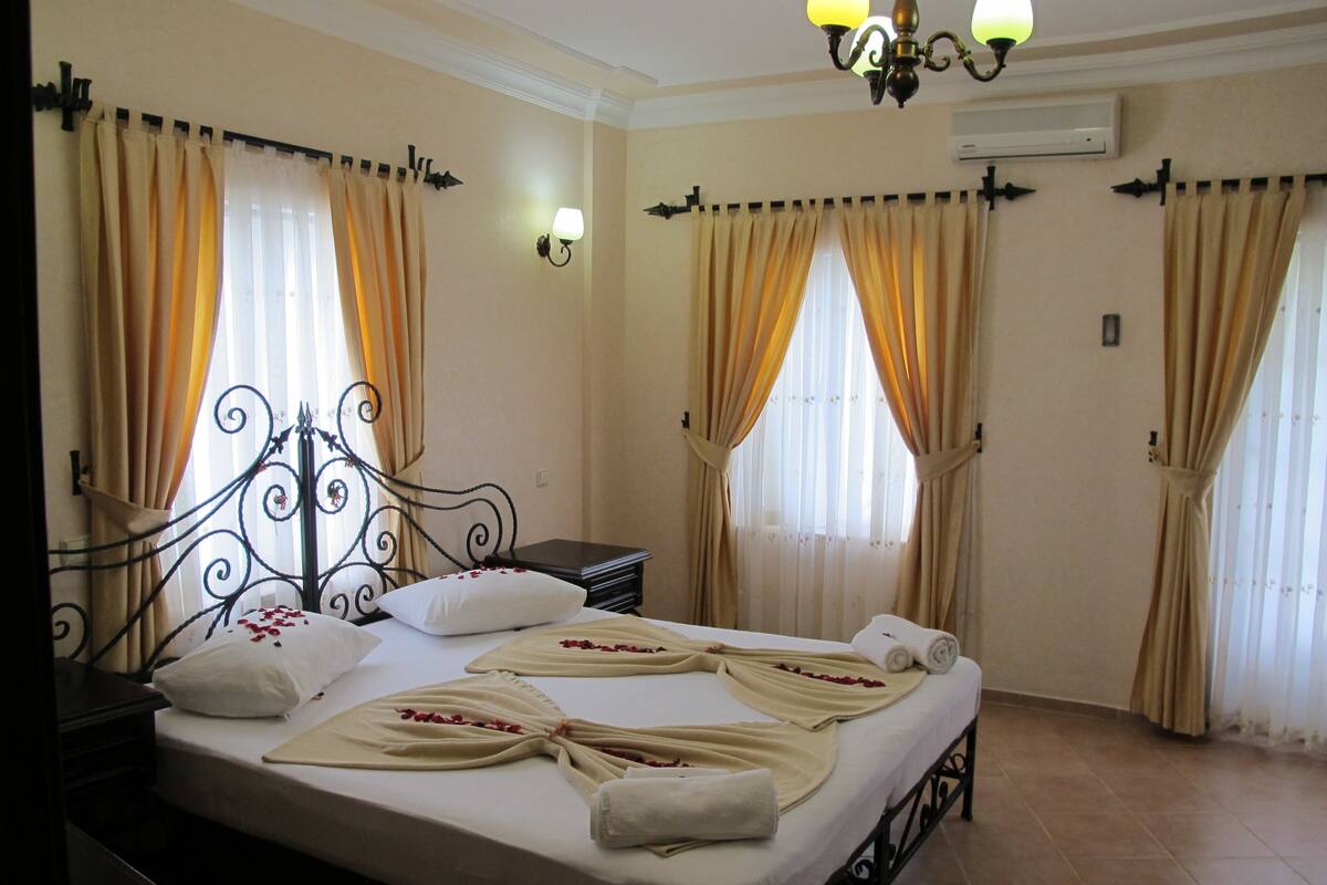 A hotel room with a bed, curtains, a nightstand, and a chandelier.