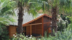 A wooden cabin with a sloped roof, surrounded by lush greenery and flowering plants. - Hemerans Anatolia Otel (Kemer)
