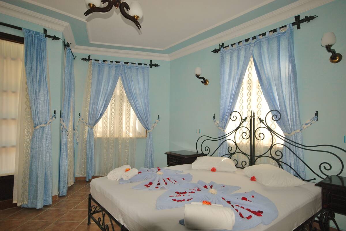 A bedroom with a bed, curtains, a chandelier, and a nightstand.