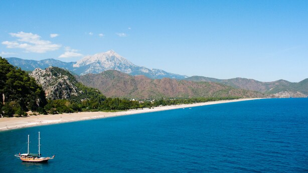 A boat on a clear blue sea with a mountain in the background and a beach on the left. - Hemerans Anatolia Otel (Kemer)