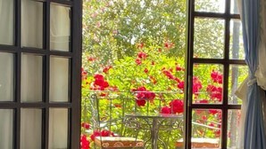 A room with a bed, a table with chairs, and a view of red flowers through a window. - Hemerans Anatolia Otel (Kemer)