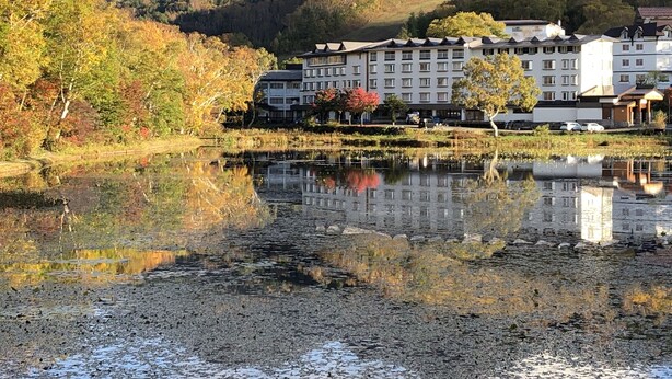 A hotel with multiple floors, a large building with a flat roof, and a reflection in a calm body of water. - Shiga Lake Hotel (Yamanouchi)