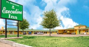 A motel with a green sign, multiple rooms, and a parking area.