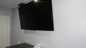 A room with a flat-screen TV mounted on the wall, a desk with a telephone, and a sign with symbols on it. - Executive Inn (Fort Stockton)