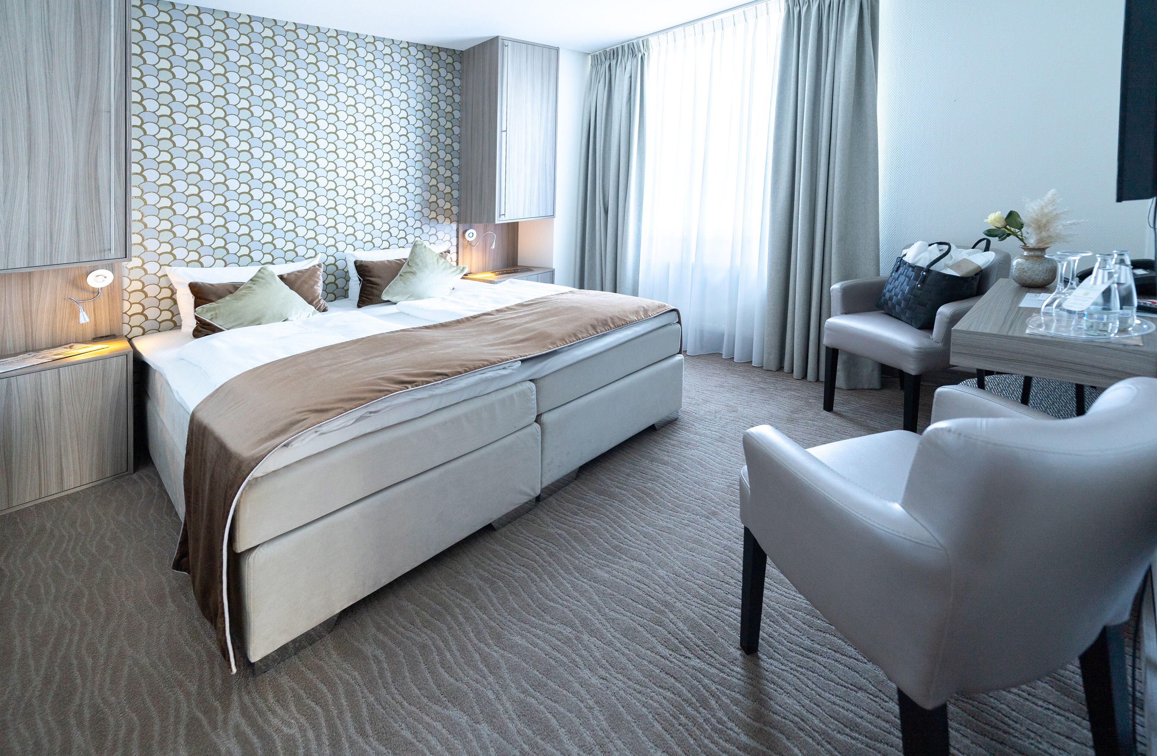 A modern hotel room with a large bed, a desk with a chair, a television, and a view of the city.