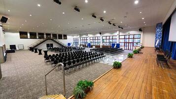 A large hall with rows of chairs, a wooden floor, and a stage with a blue backdrop.