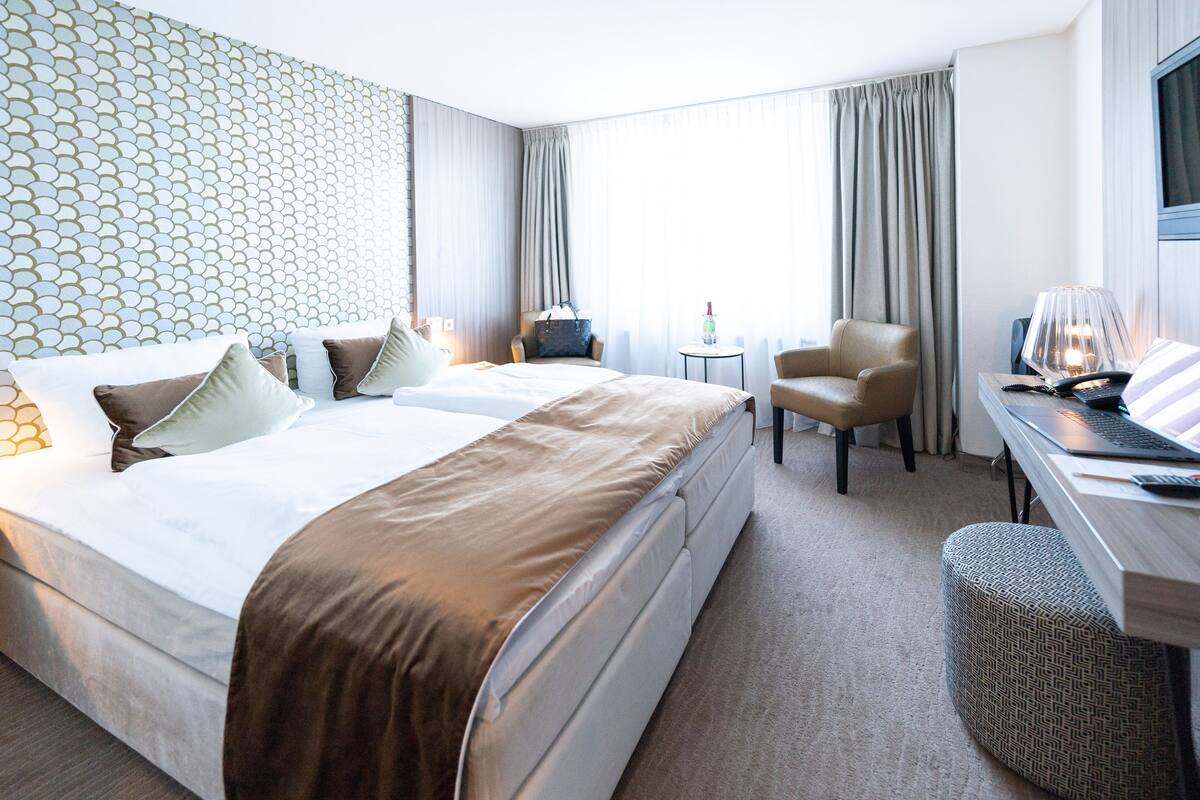 Une chambre d’hôtel avec deux lits, un bureau avec une lampe, une chaise et une petite table sur laquelle se trouve une bouteille.