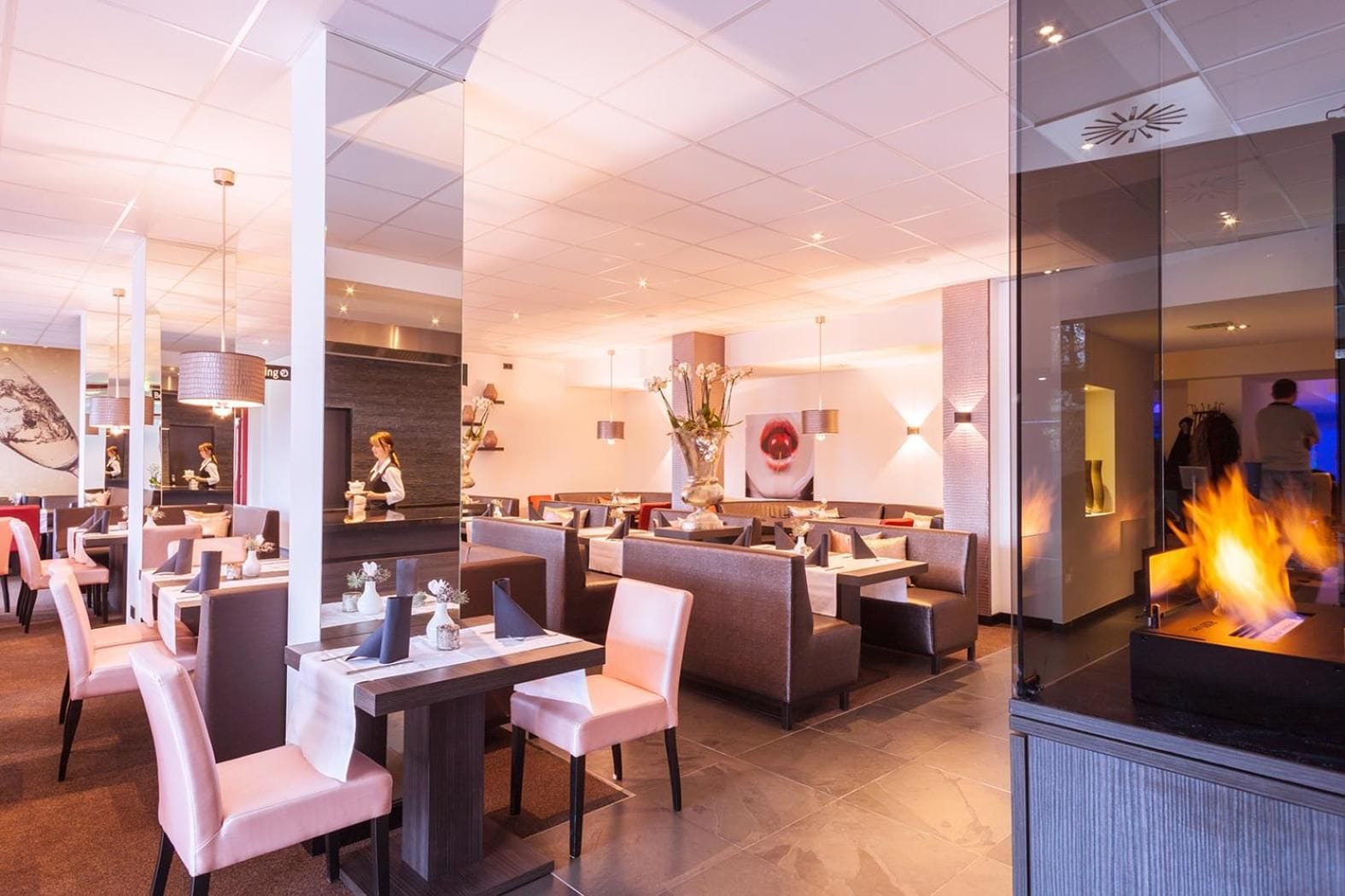 A modern restaurant with multiple dining areas, a central fire feature, and a contemporary interior design.