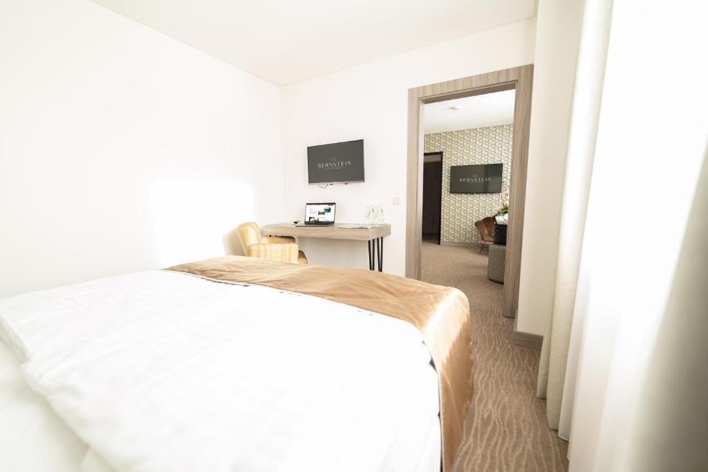 Una habitación de hotel con cama, escritorio y laptop, y televisor en la pared.