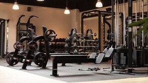 Uma academia com diversos equipamentos de exercício, luminárias pendentes e um duto com a inscrição 'FUNKTIONALITÄT'.