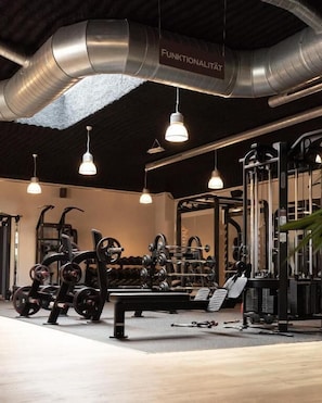 A gym with various exercise equipment, hanging lights, and a visible duct labeled 'FUNKTIONALITÄT'. - Bernstein B&B (Stassfurt)