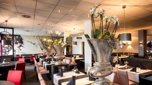 A restaurant with tables set for dining, large vases with flowers, and a modern ceiling design. - Bernstein B&B (Stassfurt)