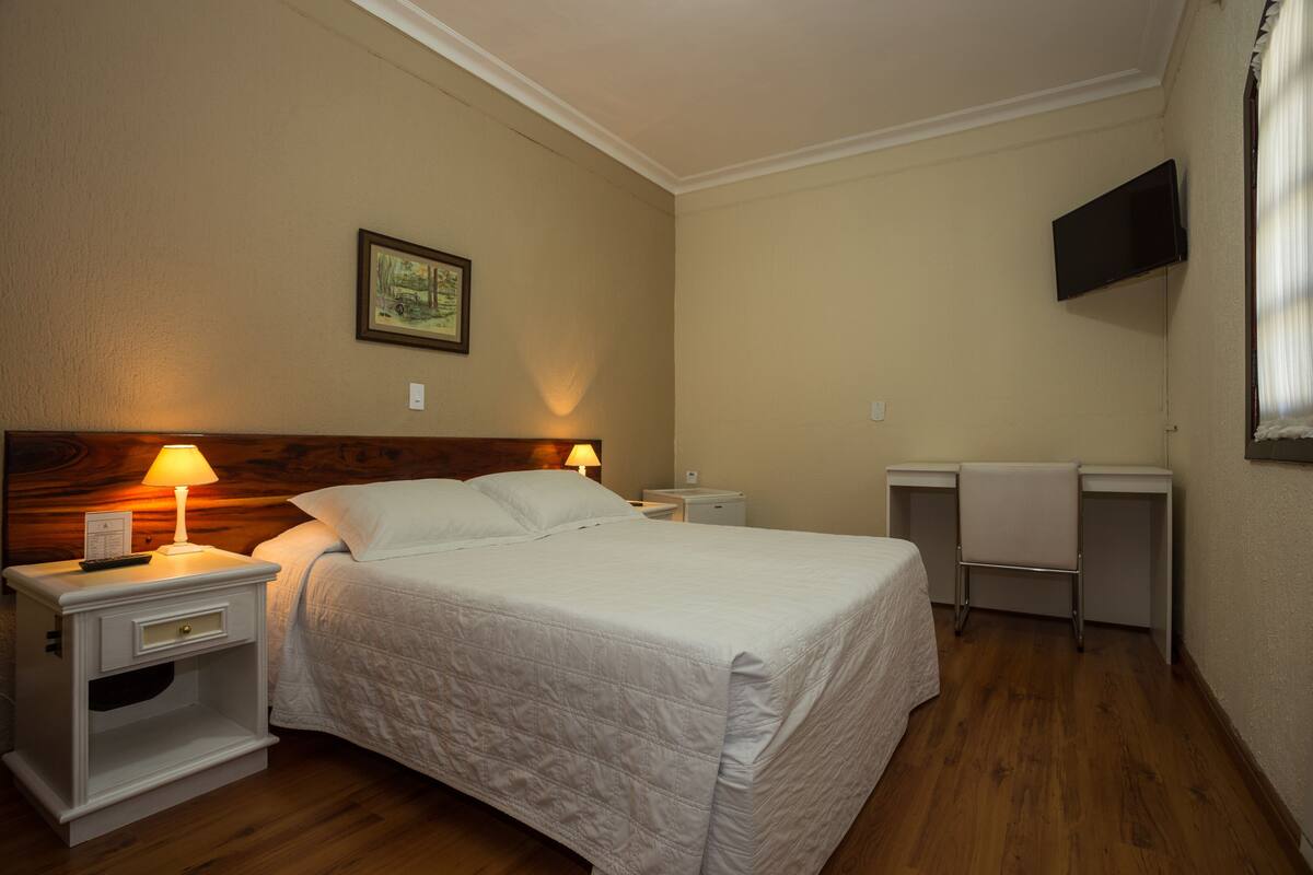 A neatly arranged hotel room with a single bed, bedside tables, a TV mounted on the wall, and a framed picture on the wall.