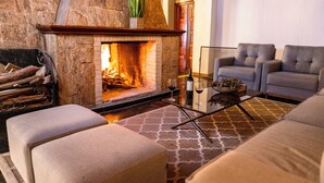 A cozy living room with a stone fireplace, comfortable seating, and a coffee table with wine glasses. - Hotel Leão da Montanha (Campos do Jordão)