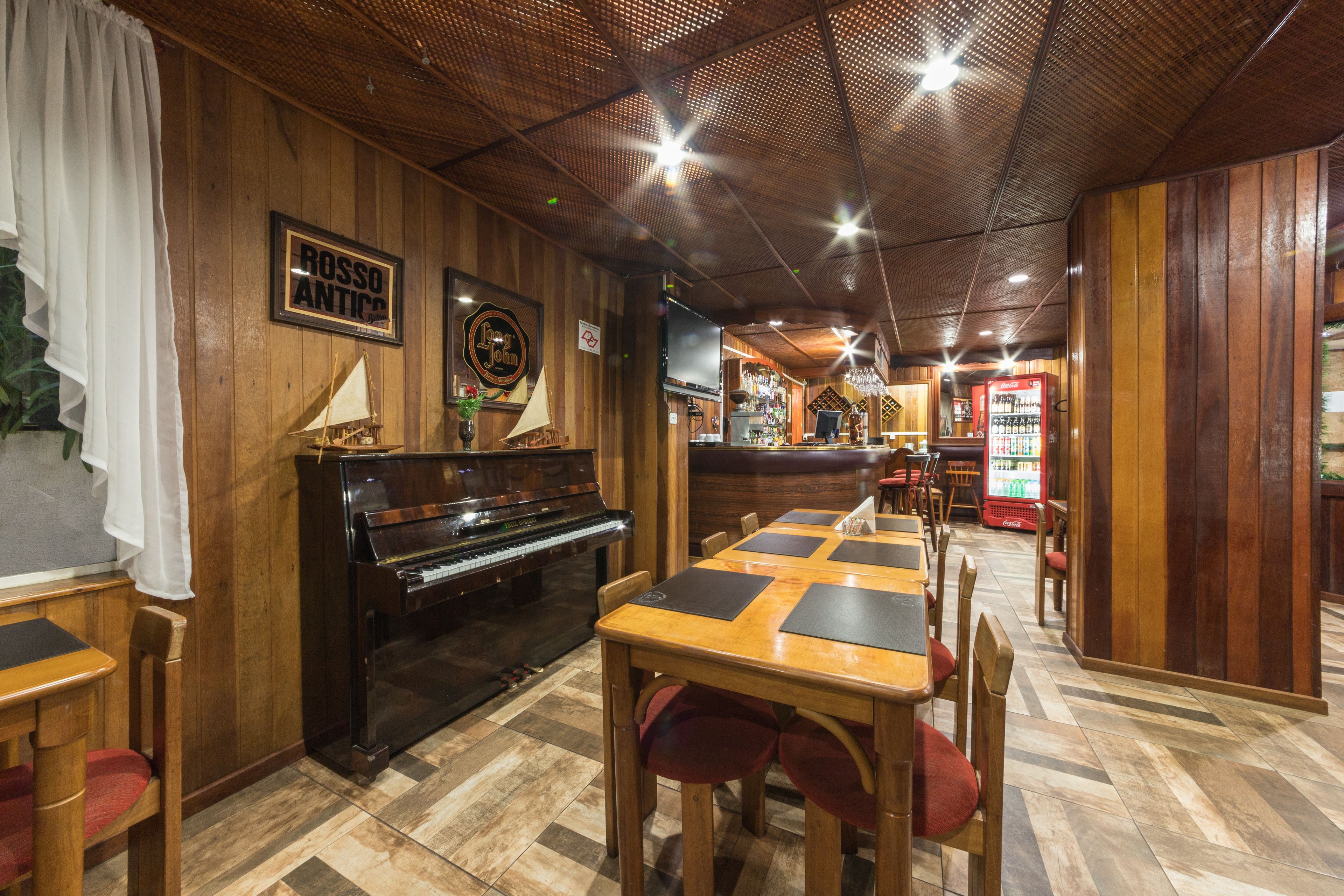 A restaurant interior with wooden paneling, a piano, tables with red cushioned chairs, and a bar area.