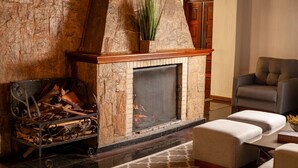 A stone fireplace with a mantel, a fire, and a log rack. There is a cushioned bench and a patterned rug. - Hotel Leão da Montanha (Campos do Jordão)
