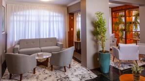 A modern living room with a grey sofa, two armchairs, a coffee table, and a large potted plant. - Hotel Leão da Montanha (Campos do Jordão)