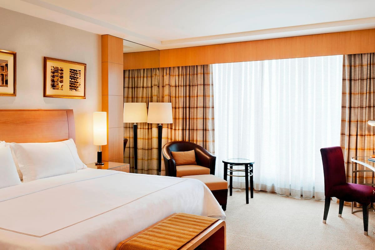 A hotel room with a large bed, two chairs, a small table, and a lamp.