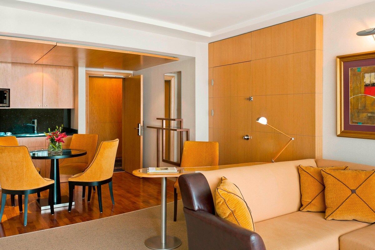 A modern hotel room with a dining area, a sofa, and a kitchen.