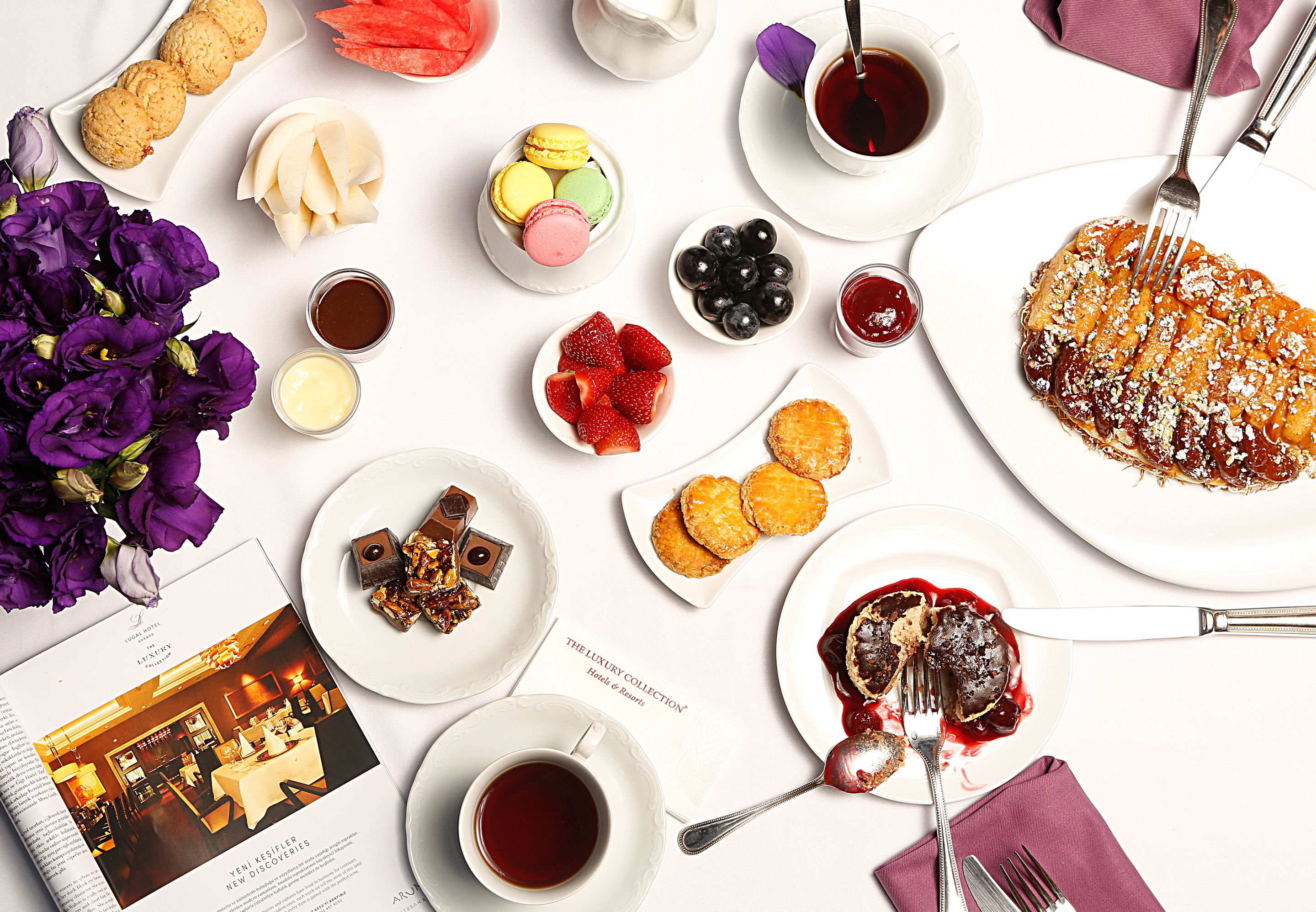 A variety of desserts and pastries on plates, a book, and a cup of tea on a white table.