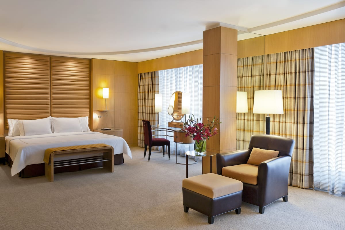 A hotel room with a large bed, a desk with a chair, a small table with a vase, and a sofa.